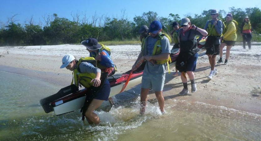 A group of people carry a kayak into the water from a sandy beach